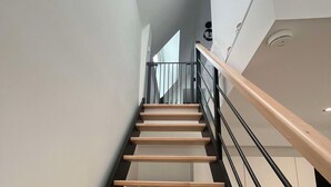 A modern staircase with wooden steps and metal railings, leading to a laundry room with a washing machine and dryer.