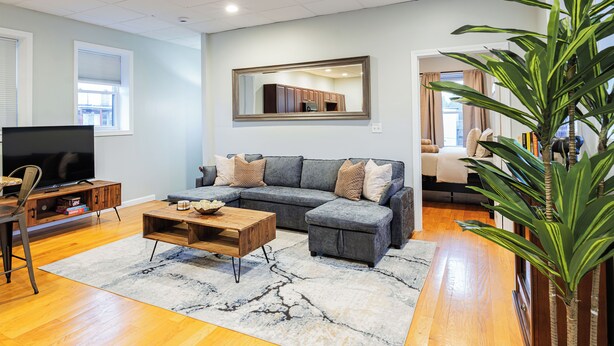 A living room with a sectional sofa, a coffee table, a TV, and a large mirror on the wall. - Boston Getaway, Close to Airport (Boston)