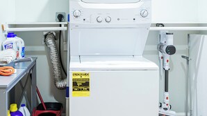 A compact, white laundry room with a front-loading washing machine, a drying machine, and a shelf with cleaning supplies. - Boston Getaway, Close to Airport (Boston)