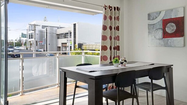 Un'area pranzo moderna con tavolo e sedie, vista sulla città attraverso ampie finestre e un'opera d'arte astratta appesa al muro.
