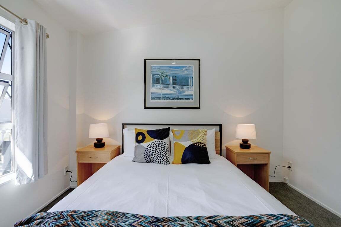 A hotel room with a bed, two bedside tables with lamps, a framed picture on the wall, and a window with curtains.