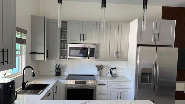 Een moderne keuken met witte kasten, een centraal eiland, roestvrijstalen apparatuur en hanglampen.