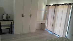 Een slaapkamer met een bed, een kledingkast, een bureau met spiegel en een raam met gordijnen.