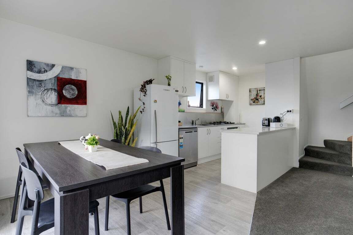 A modern kitchen with white cabinets, a central island, and a dining area with a dark wooden table and chairs.