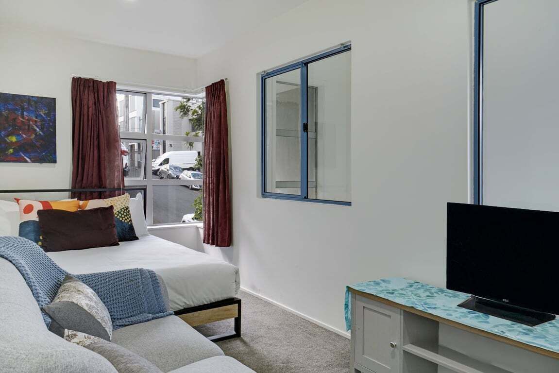 A bedroom with a bed, a sofa, a TV, and a window.