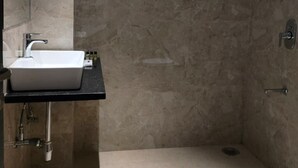 A modern bathroom with a white sink, a shower, and marble walls. - Heaven X Inn Hotel (Indore)