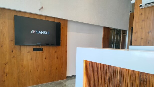 A reception area with a wooden panel wall, a mounted television displaying 'SANSUI', and a marble floor. - Heaven X Inn Hotel (Indore)
