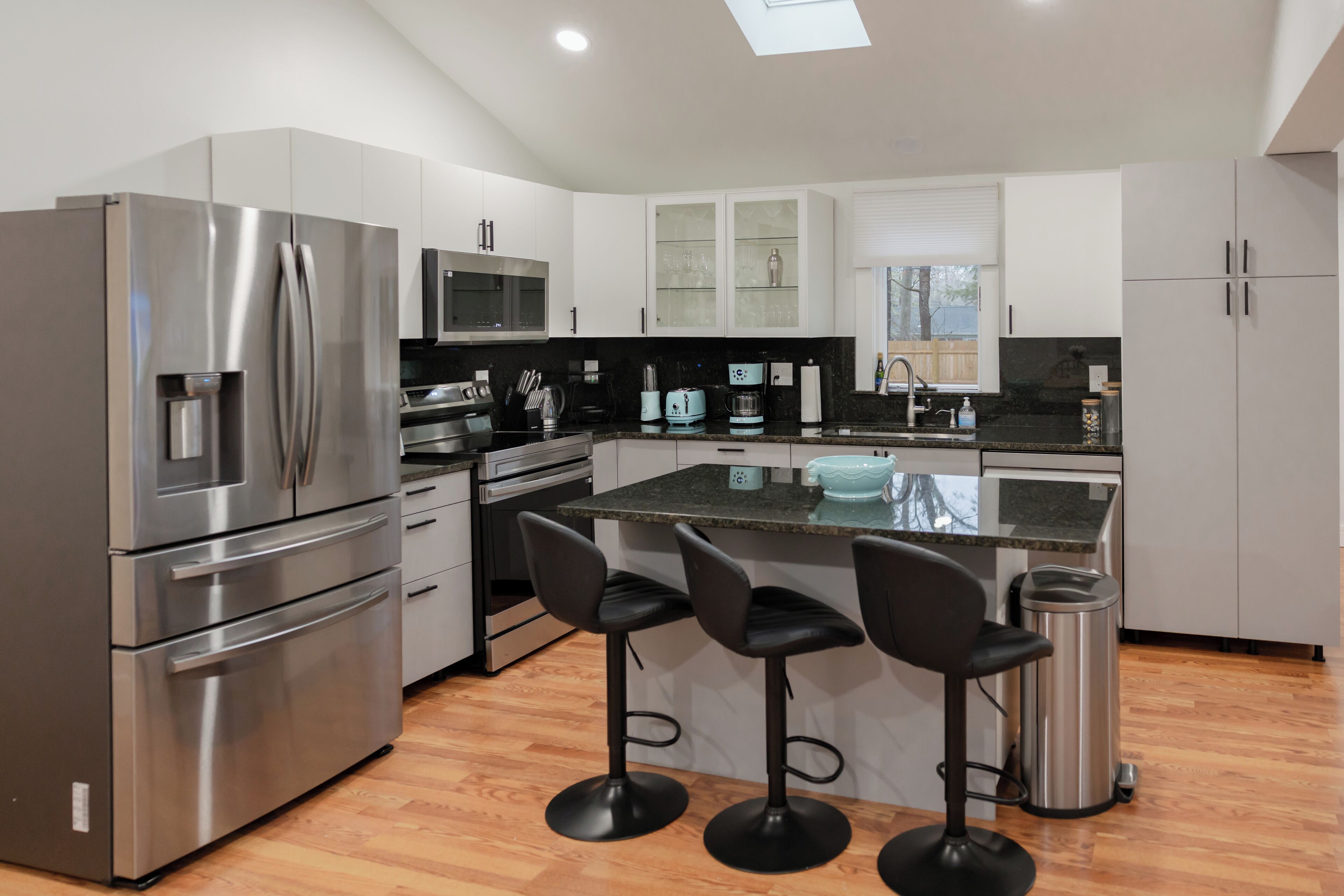 A modern kitchen with stainless steel appliances, white cabinetry, and a central island with bar stools.