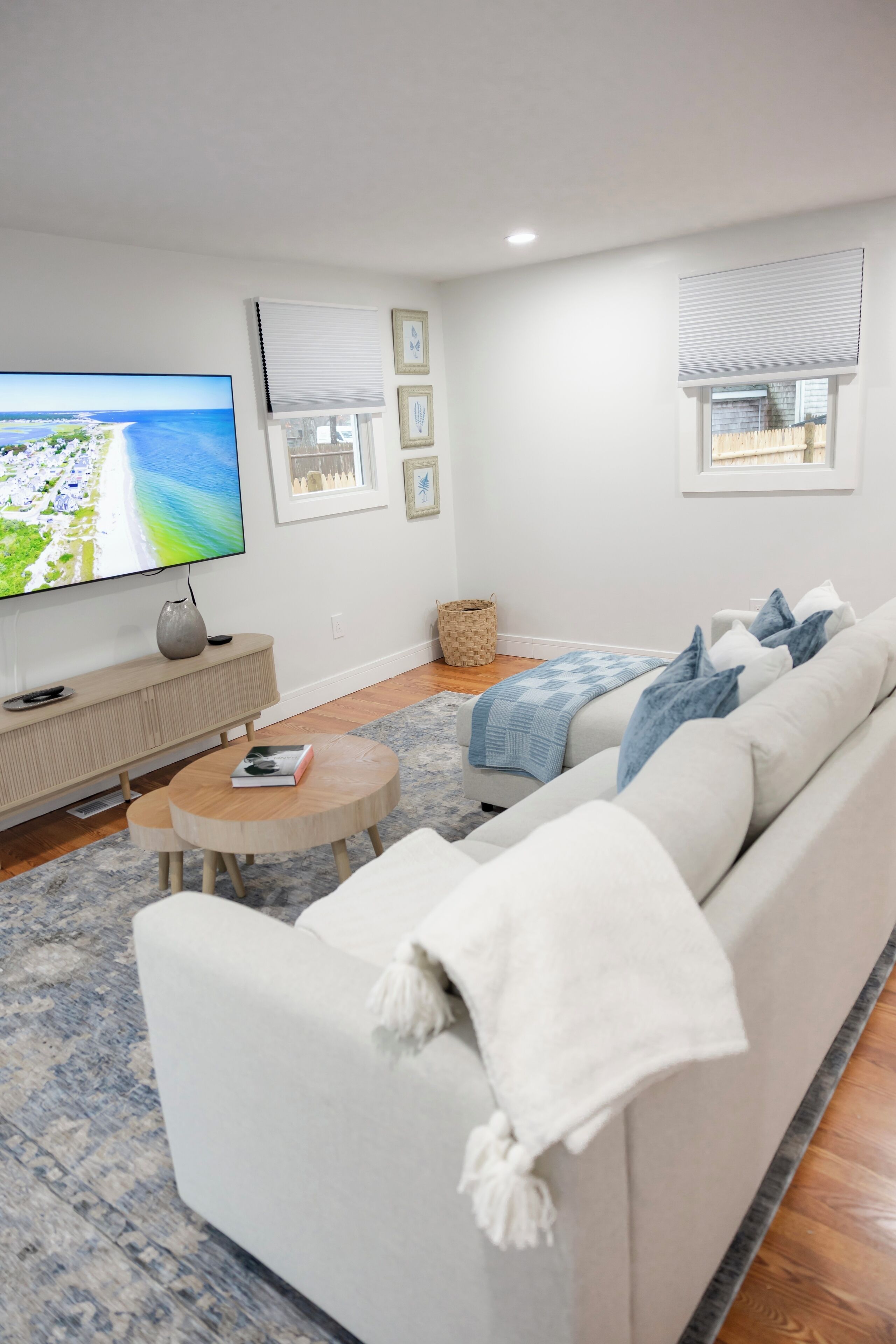 A modern living room with a large flat-screen TV, a beige sofa, a round coffee table, and a blue patterned rug.