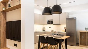 Una cucina moderna con zona pranzo, caratterizzata da un tavolo in legno, sedie nere e illuminazione a sospensione.