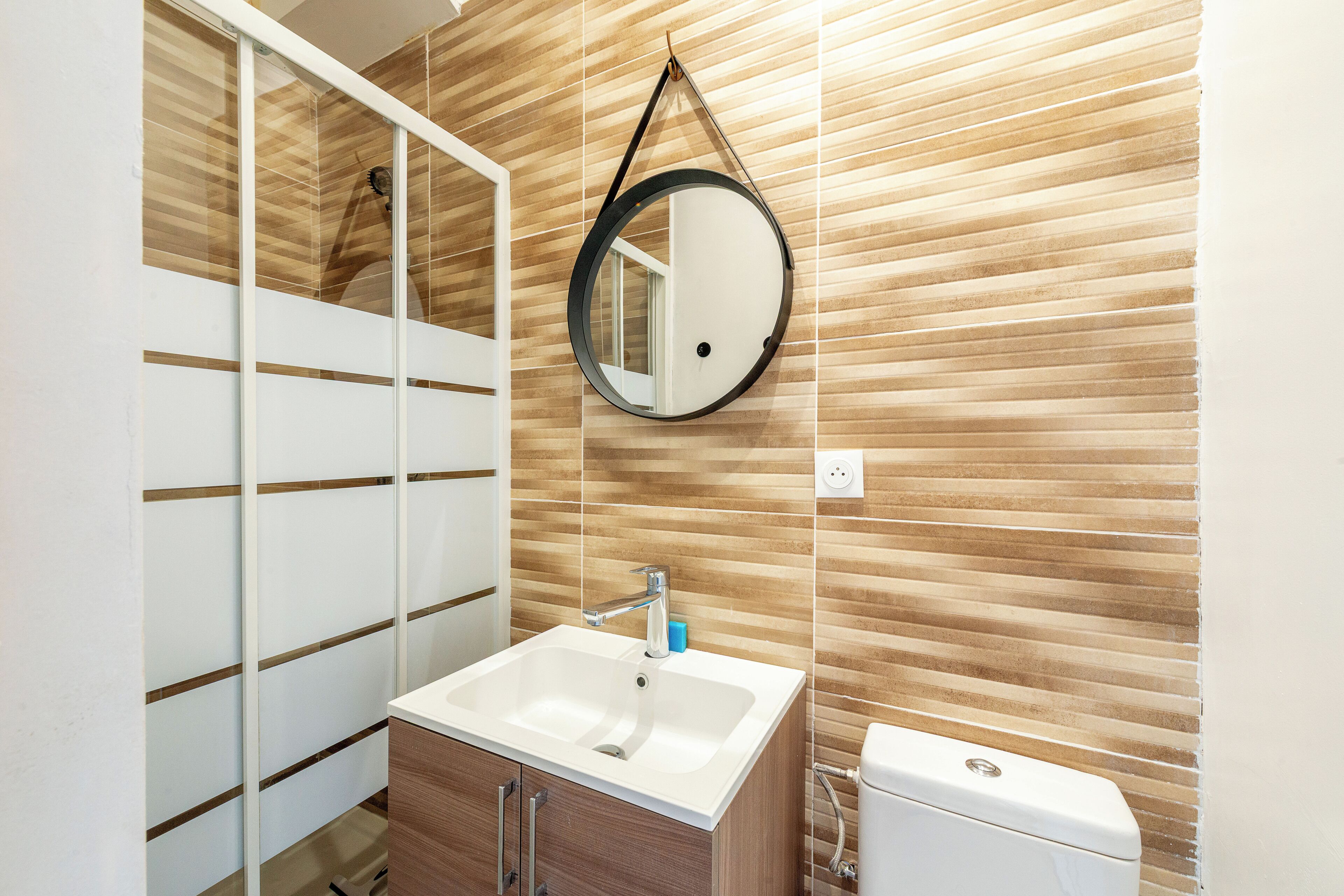 Een badkamer met een houten wand, een ronde spiegel, een witte wastafel en een toilet.