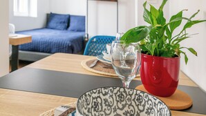 Zona pranzo con tavolo, vaso rosso contenente una pianta, bicchiere d'acqua e un letto sullo sfondo.