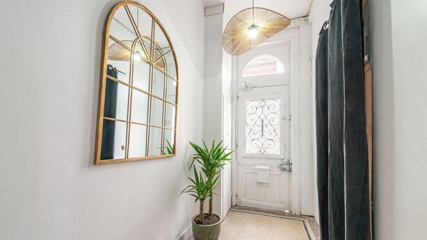 Un corridoio con un grande specchio, una pianta in vaso, una porta con un pannello di vetro decorativo e un lampadario.