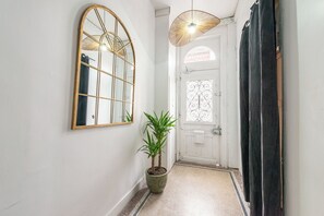 A hallway with a large mirror, a potted plant, a door with a decorative glass panel, and a hanging light fixture. - Lovely, bright studio just 1 minute from the station (Cambrai)