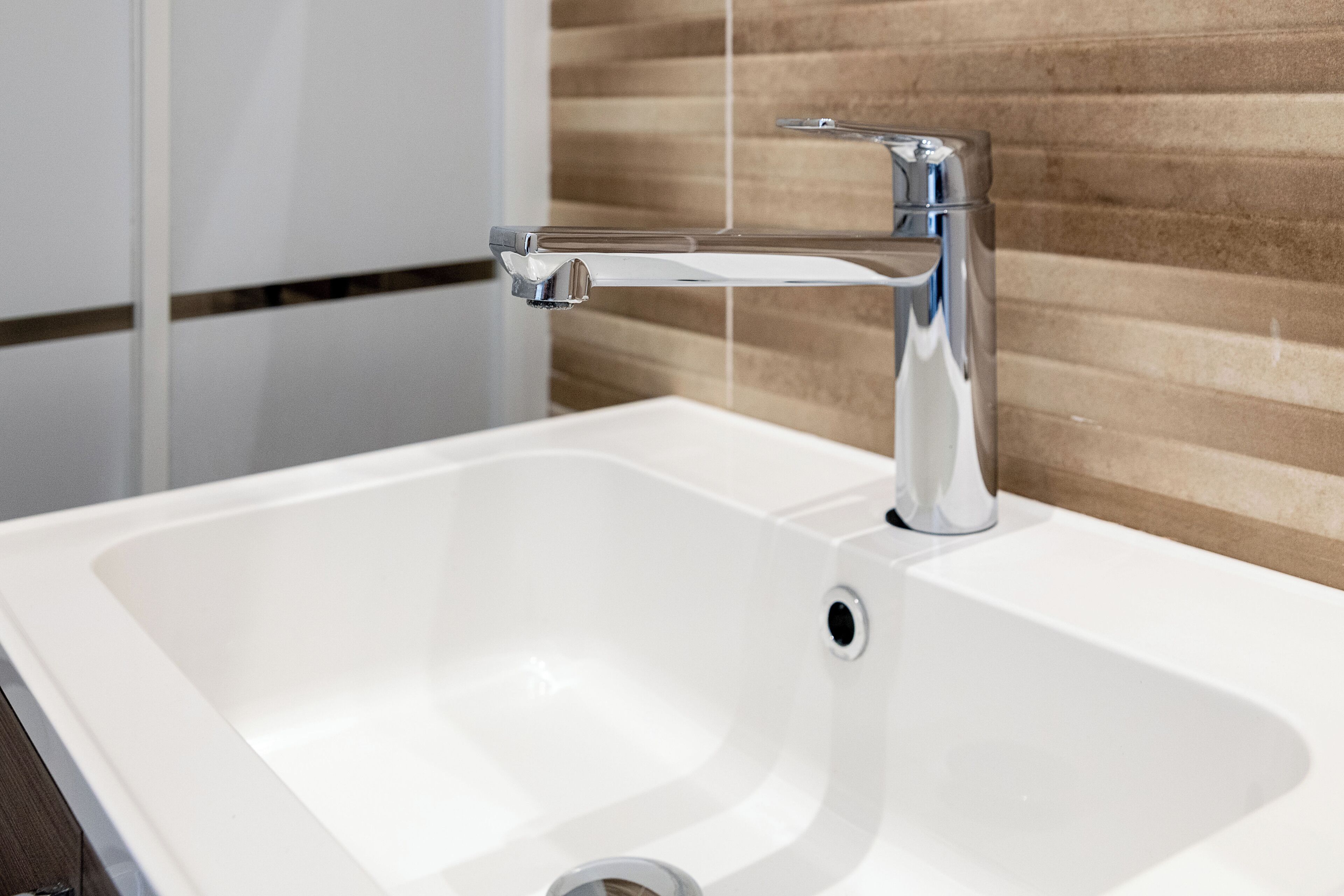 A modern bathroom with a chrome faucet, a white sink, and a wooden wall panel.