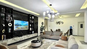 A modern living room with a flat-screen TV, a round coffee table, and a sofa set. - ASIO HOMES (Lekki)