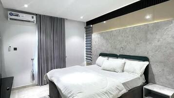 Un dormitorio moderno con una cama grande, una mesita de noche, un banco empotrado y un aire acondicionado instalado en la pared.