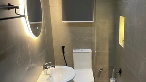 A modern bathroom with a pedestal sink, a toilet, and a wall-mounted mirror with integrated lighting.