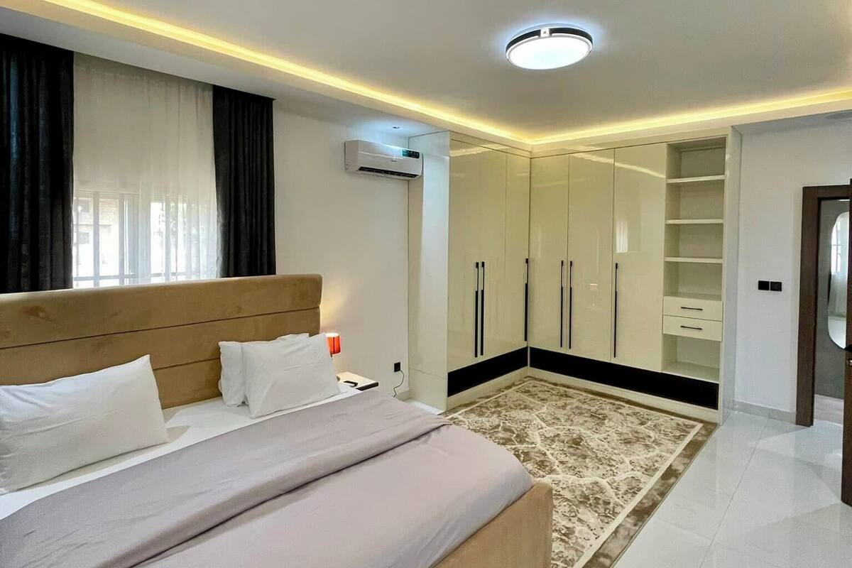 A modern bedroom with a large bed, a walk-in closet, and an air conditioning unit.