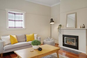A living room with a sofa, a coffee table, a floor lamp, a fireplace, and a window with decorative glass.