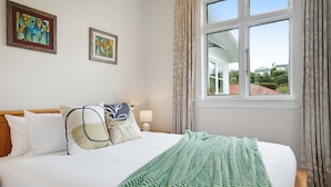 Een hotelkamer met een bed, twee schilderijen aan de muur, een raam met gordijnen en uitzicht op buiten.