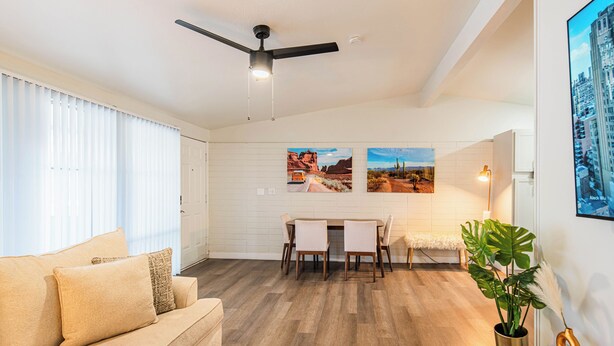 Een woonkamer met een bank, een eettafel met stoelen, een plafondventilator en twee ingelijste foto's aan de muur.
