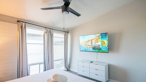 Hotelkamer met een bed, een plafondventilator, een aan de muur bevestigde televisie en een raam met gordijnen.