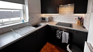 A compact kitchen with a window, a microwave, a sink, and black cabinets. - Apartment - Sleeps4 - Glasgowairport 10 Mins Drive (Renfrew)