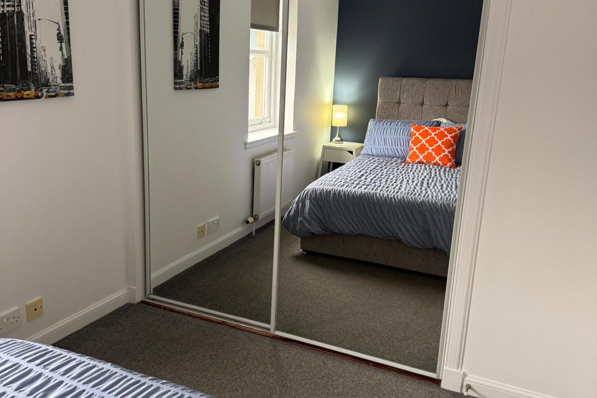 A bedroom with a bed, a nightstand, a lamp, and a mirror.