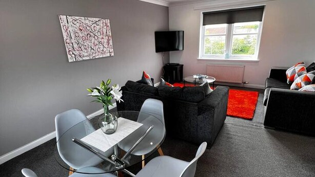 A modern living room with a glass dining table, grey chairs, a black sofa, and a red rug. - Apartment - Sleeps4 - Glasgowairport 10 Mins Drive (Renfrew)