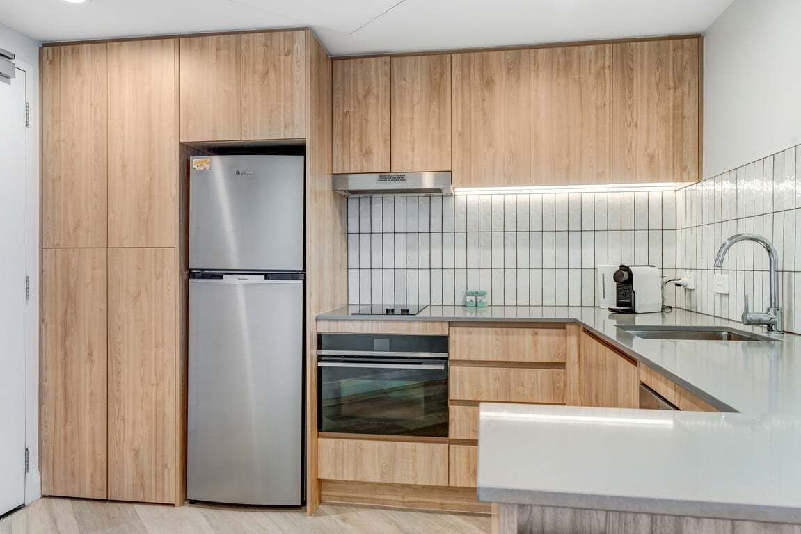 Een moderne keuken met houten kastjes, roestvrijstalen apparatuur en een betegelde achterwand.