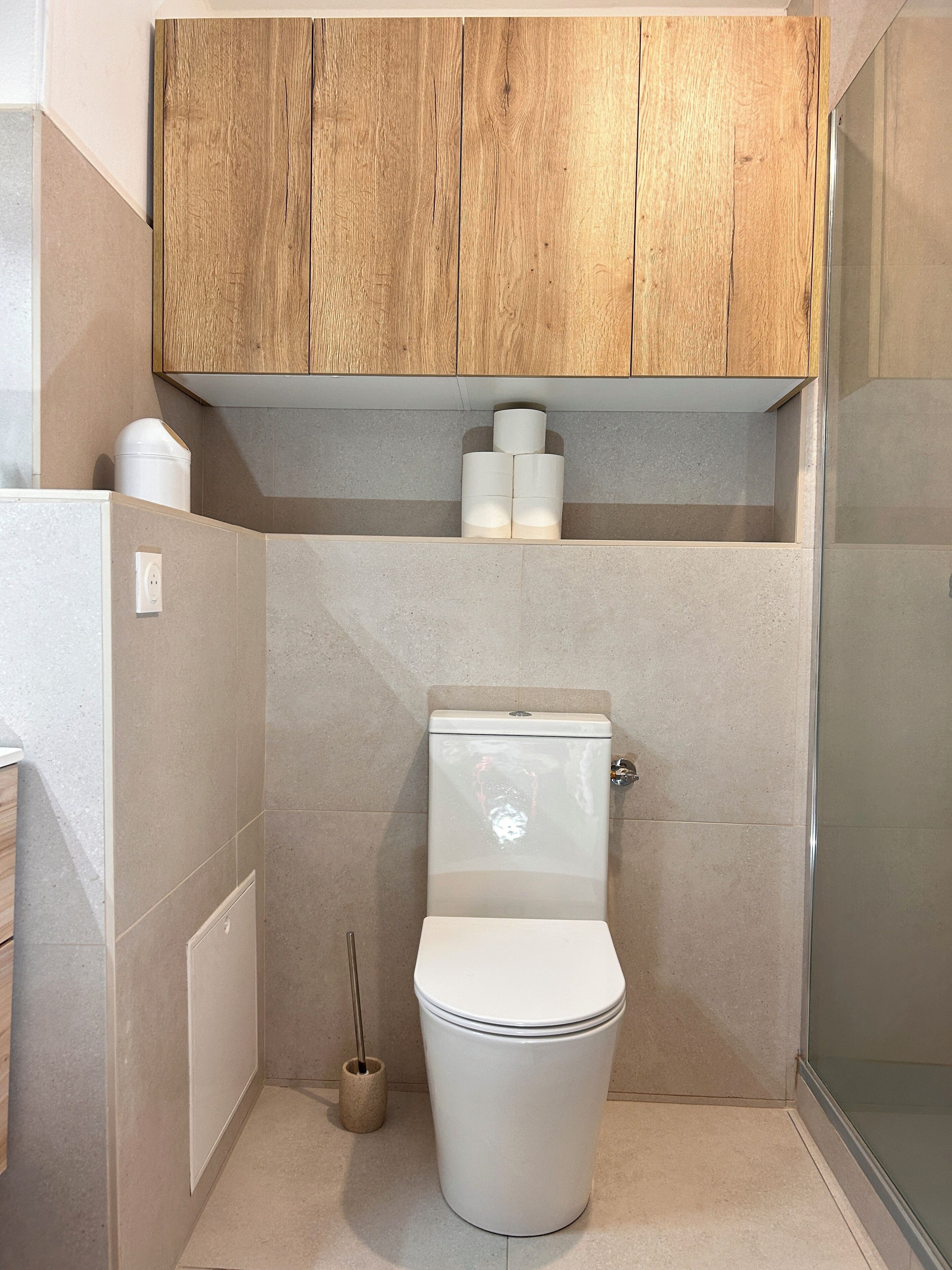 Une salle de bain moderne avec des toilettes, un meuble en bois au-dessus et un porte-rouleau de papier toilette.