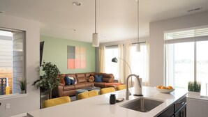 Une cuisine moderne avec un îlot central, un coin repas avec des chaises jaunes et un salon doté d’un canapé en cuir marron.