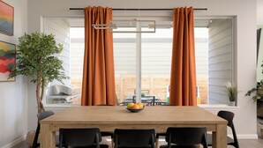 Un coin repas avec une table en bois, des chaises noires et des rideaux orange.