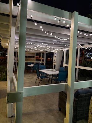 An outdoor patio area with tables and chairs, string lights overhead, and a view of the city at night. - Penguins on the Beach | 2BR Steps to Beach & Downtown w/pool | Unit G (Cocoa Beach)