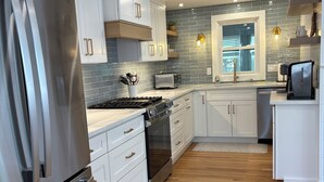 Cozinha moderna com eletrodomésticos de aço inoxidável, armários brancos e piso de madeira.