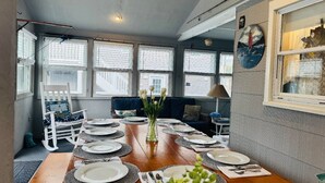 Un'area pranzo con un tavolo di legno apparecchiato per sei persone, una poltrona a dondolo bianca e un divano blu.