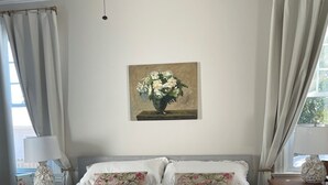 Ein ordentlich bezogenes Bett mit floralen Kissen, ein Blumenbild an der Wand und ein Deckenventilator.