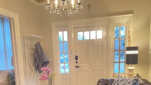 Ein Wohnzimmer mit braunem Ledersofa, einer Kristallleuchtre, einer weißen Tür und einem kleinen Tisch mit Schale und Pflanze.