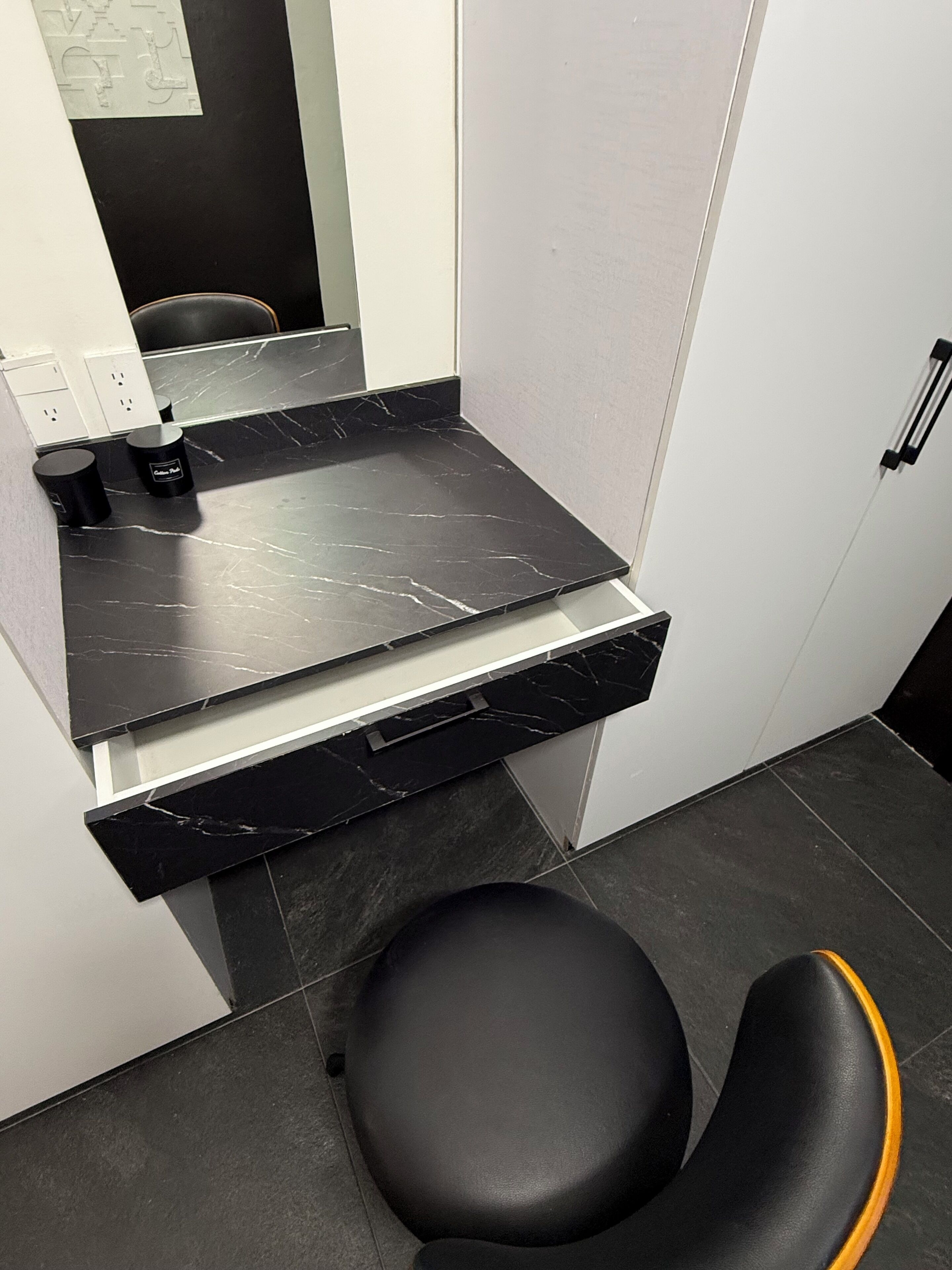 A bathroom with a black marble countertop, a black sink, and a black chair with an orange accent.