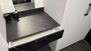 Bany amb taulell de marbre negre, un lavabo negre i una cadira negra amb un toc taronja.
