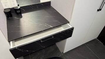 A bathroom with a black marble countertop, a black sink, and a black chair with an orange accent.