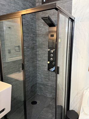 A modern shower enclosure with a control panel, dark textured walls, and a marble-tiled floor. - APARTMENT IN THE HEART OF OAXACA IN FRONT OF THE LOCAL MARKET, EVERYTHING CLOSE BY! (Oaxaca de Juárez)