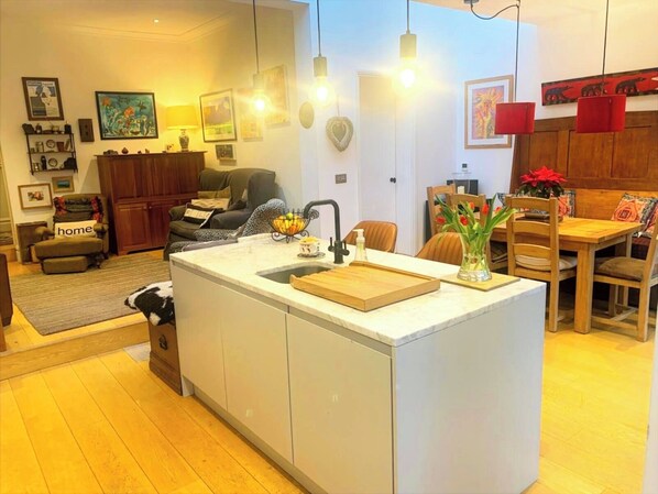 A modern kitchen with a central island, white cabinetry, and a dining area with wooden furniture. - Perfect 3-bedroom Edwardian town house in Bath for a home from home getaway (Bath)