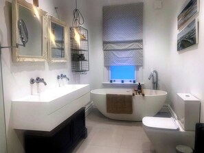 A modern bathroom with two sinks, a bathtub, and a toilet. There are mirrors above the sinks, a window with a view, and a towel rack. - Perfect 3-bedroom Edwardian town house in Bath for a home from home getaway (Bath)
