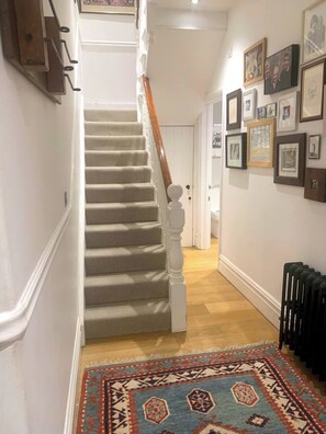 Eine Treppe mit einer Holzhandläufe, mit Teppich belegten Stufen und einem gemusterten Teppich am Fuß.