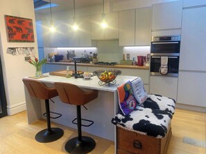 Eine moderne Küche mit einer zentralen Kochinsel, Barhocker, einem Kühlschrank und einer Mikrowelle.