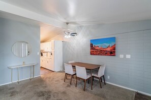 A dining area with a wooden table and chairs, a ceiling fan, and a kitchen in the background. - Dwell 1911-3 (Scottsdale)