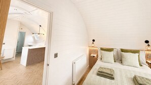 Une chambre à coucher avec un plafond incurvé, un lit doté de plusieurs oreillers, des lampes de chevet et un petit bureau avec une chaise.