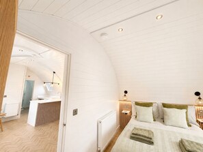 Ein Schlafzimmer mit gewölbter Decke, einem Bett mit vielen Kissen, Nachttischlampen und einem kleinen Schreibtisch mit Stuhl.